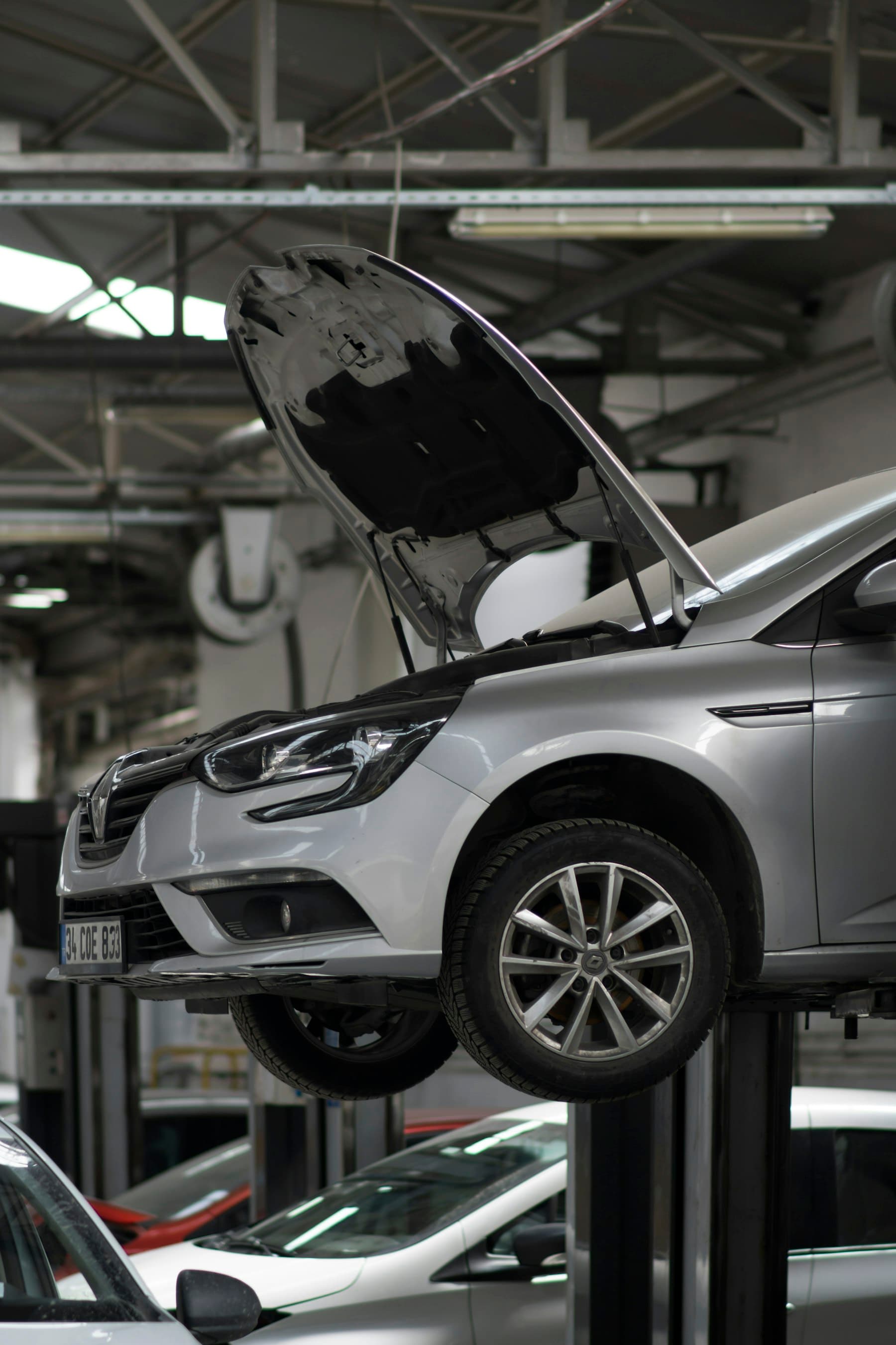 A silver hatchback with its bonnet up on a lift in a repair workshop